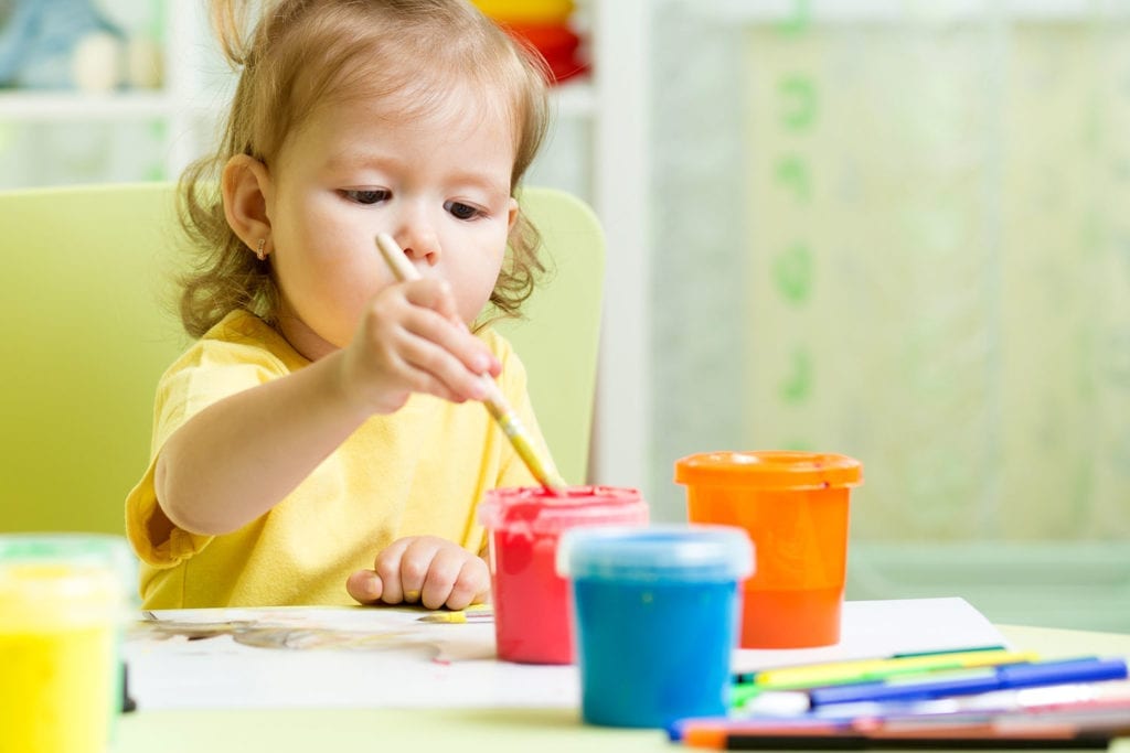 Toddler girl painting at childcare table