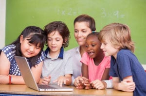 Diverse primary classroom learning to use laptop with their